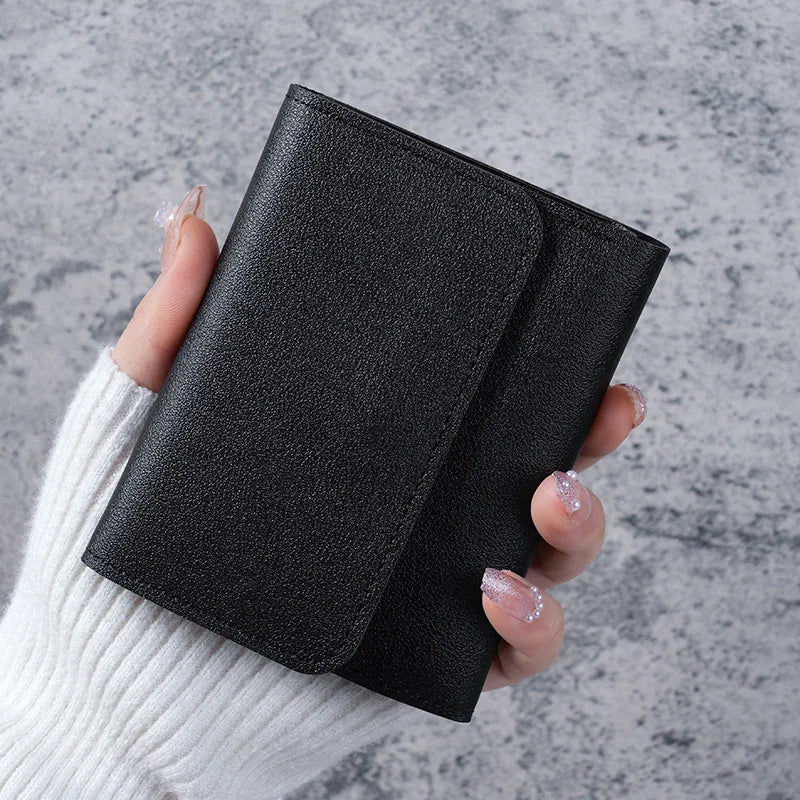 A hand holds a black slim triple-fold PU leather wallet against a gray background.
