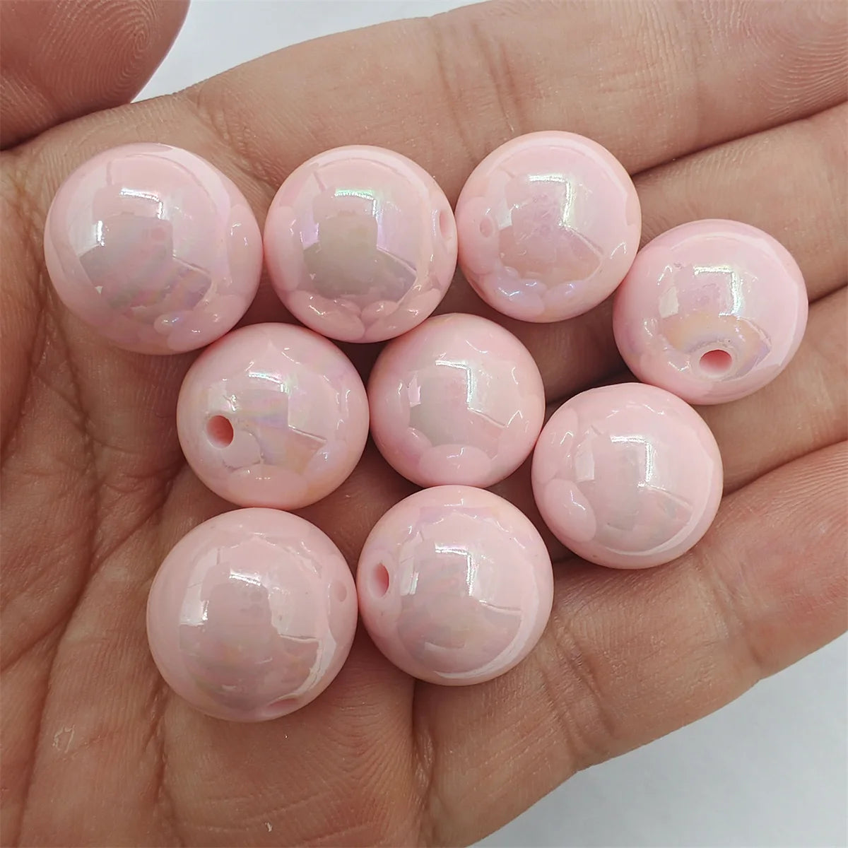 A hand holds several round, pink magic color acrylic beads for jewelry making.