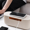 A beige cable management box with a black smartphone resting on it, next to a laptop and power cord.