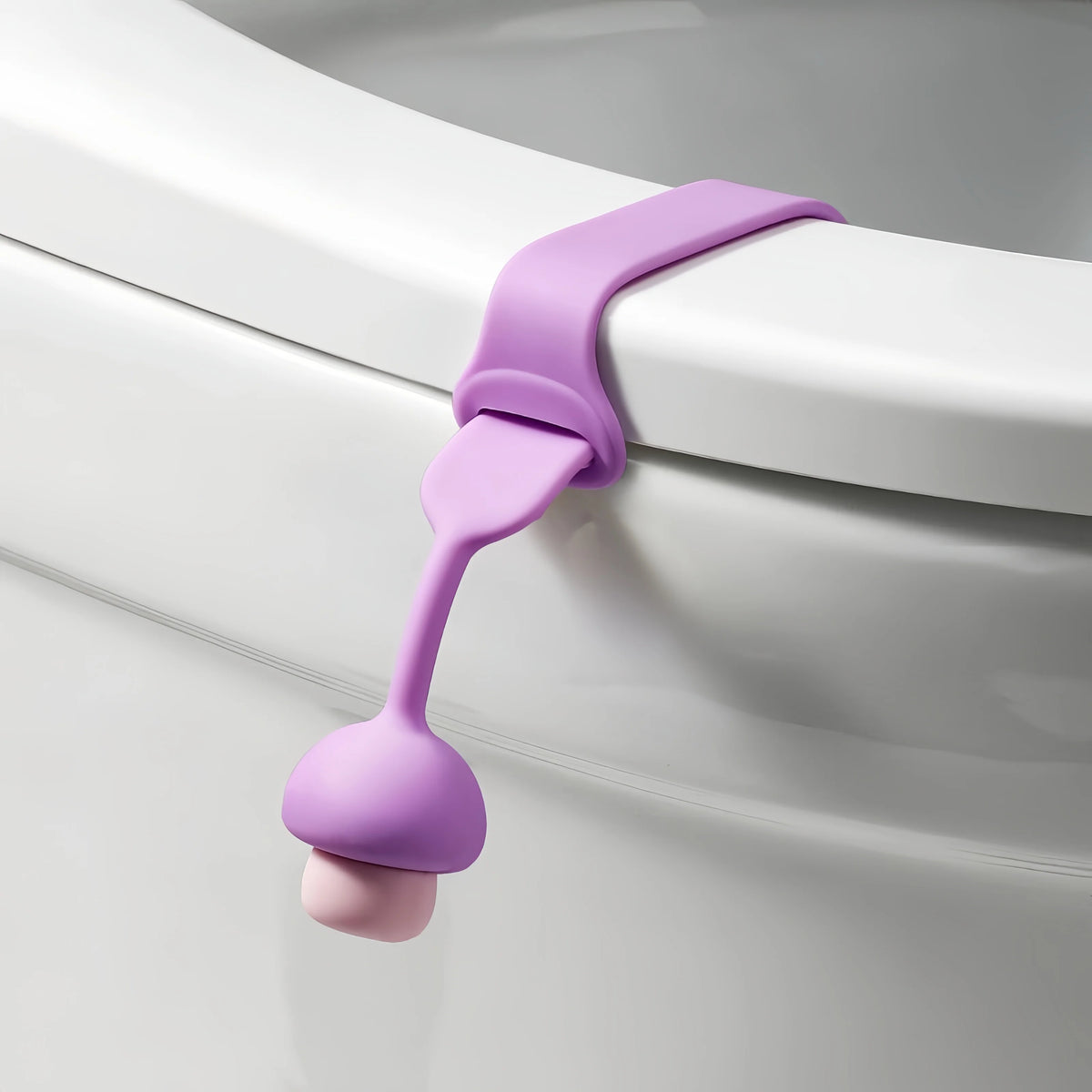A purple silicone toilet seat lifter with a pull ring is shown against a white porcelain surface.