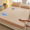 A beige fitted mattress protector is shown on a bed, with a hand touching the fabric and a blue liquid dripping onto it.