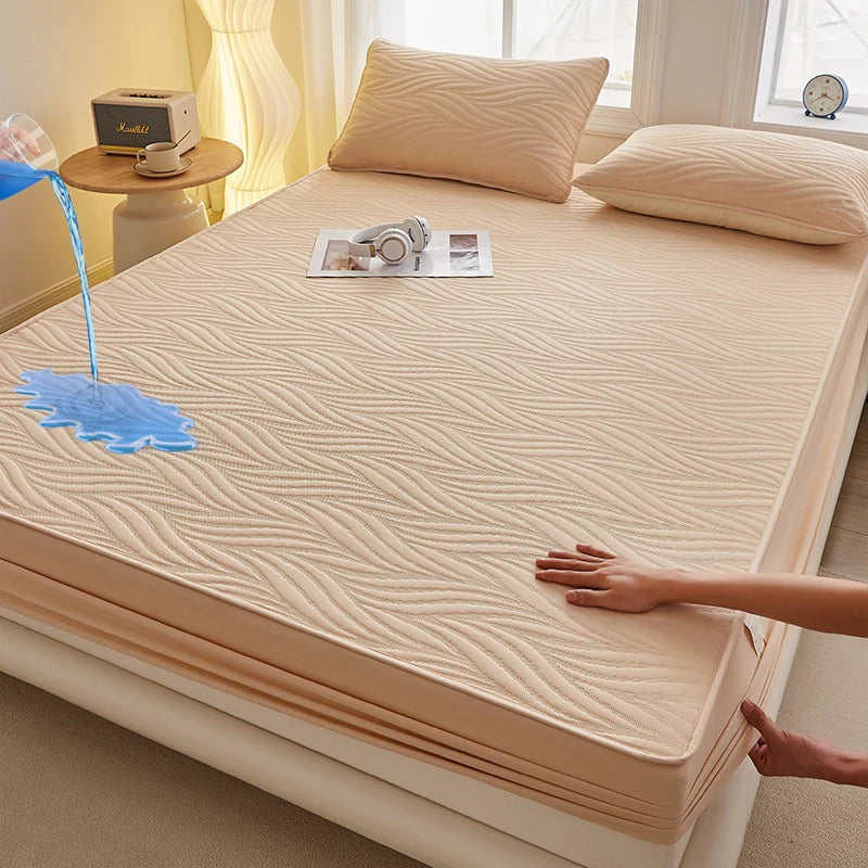 A beige fitted mattress protector is shown on a bed, with a hand touching the fabric and a blue liquid dripping onto it.