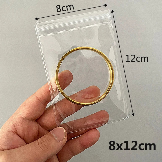 A hand holds a transparent jewelry pouch with a gold ring inside, showing its dimensions.