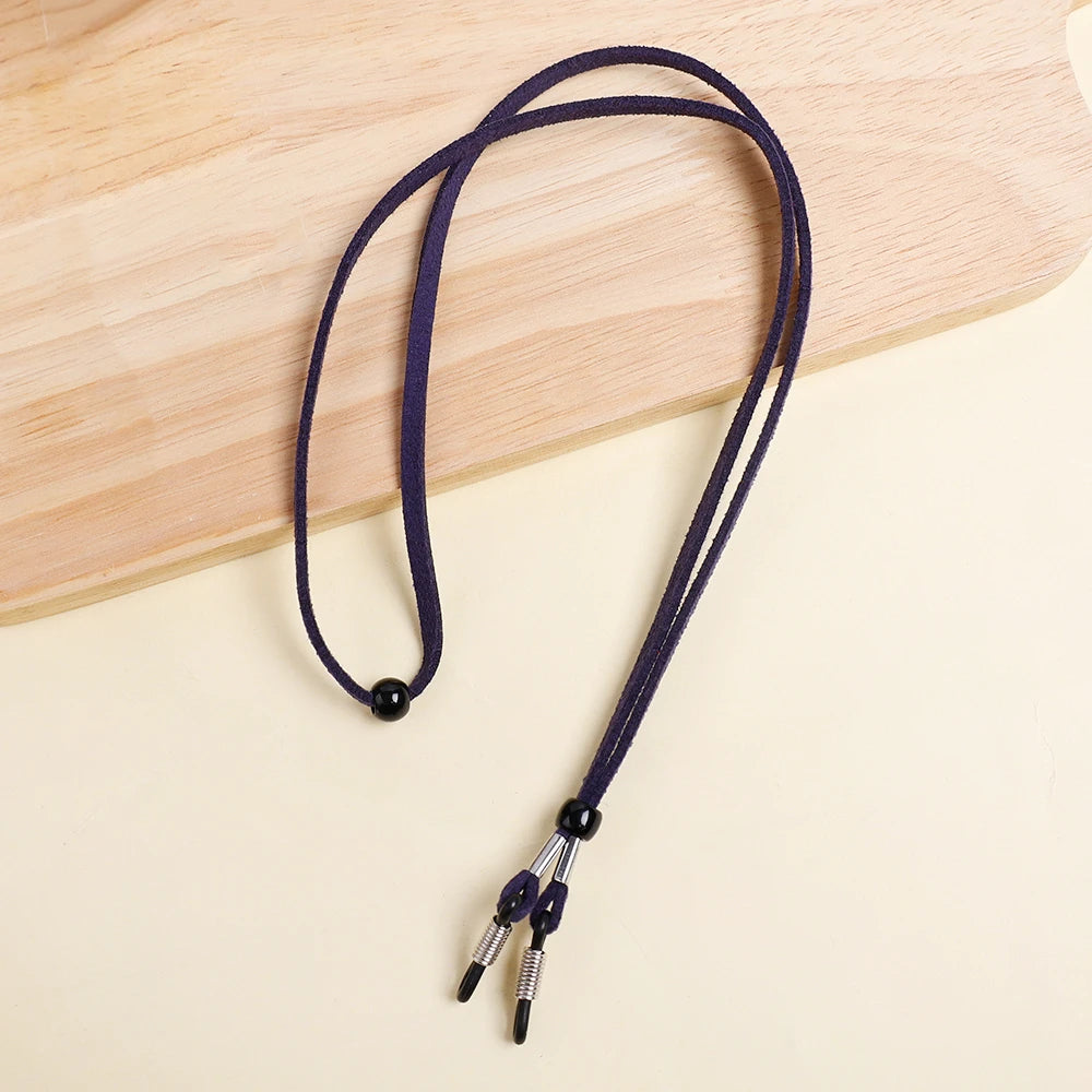 A dark navy blue adjustable lanyard for glasses is laid on a light wooden cutting board.