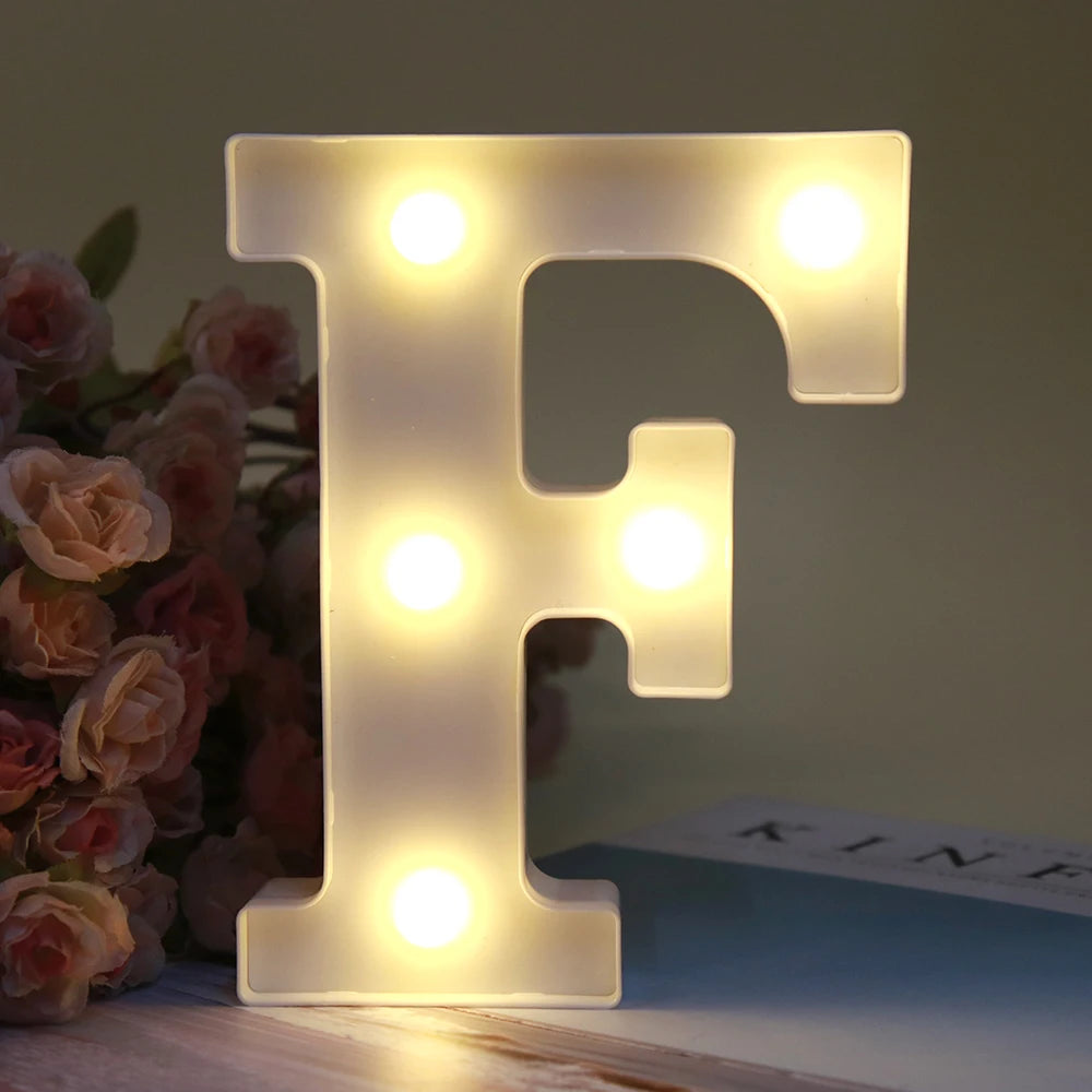 Lettre alphabet F lumineuse LED blanche, veilleuse, posée sur une surface en bois à côté de roses et d'un livre.