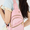 A pink quilted crossbody sling bag with a pink strap is worn by a person in a light blue top.