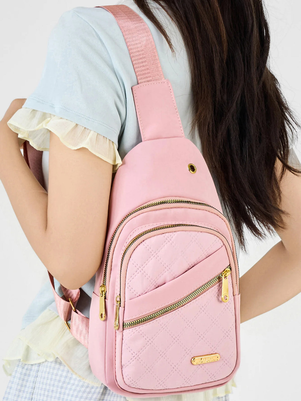 A pink quilted crossbody sling bag with a pink strap is worn by a person in a light blue top.