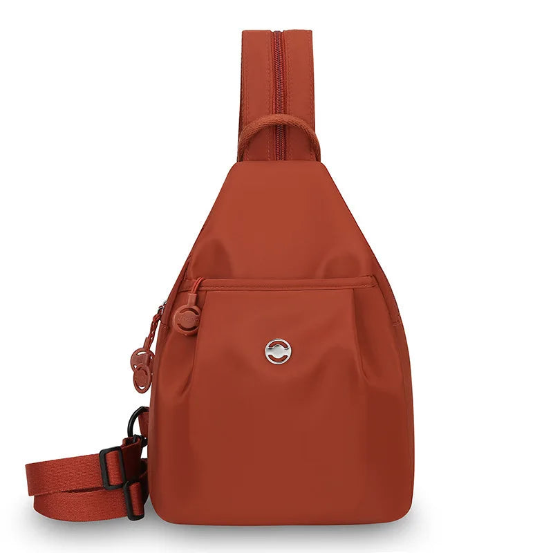 A terracotta orange women's lightweight mini backpack with a brown anti-theft chest strap.