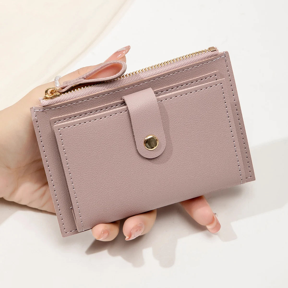 A hand holds a light pink slim PU leather card holder wallet with a gold zipper and a leather flap.