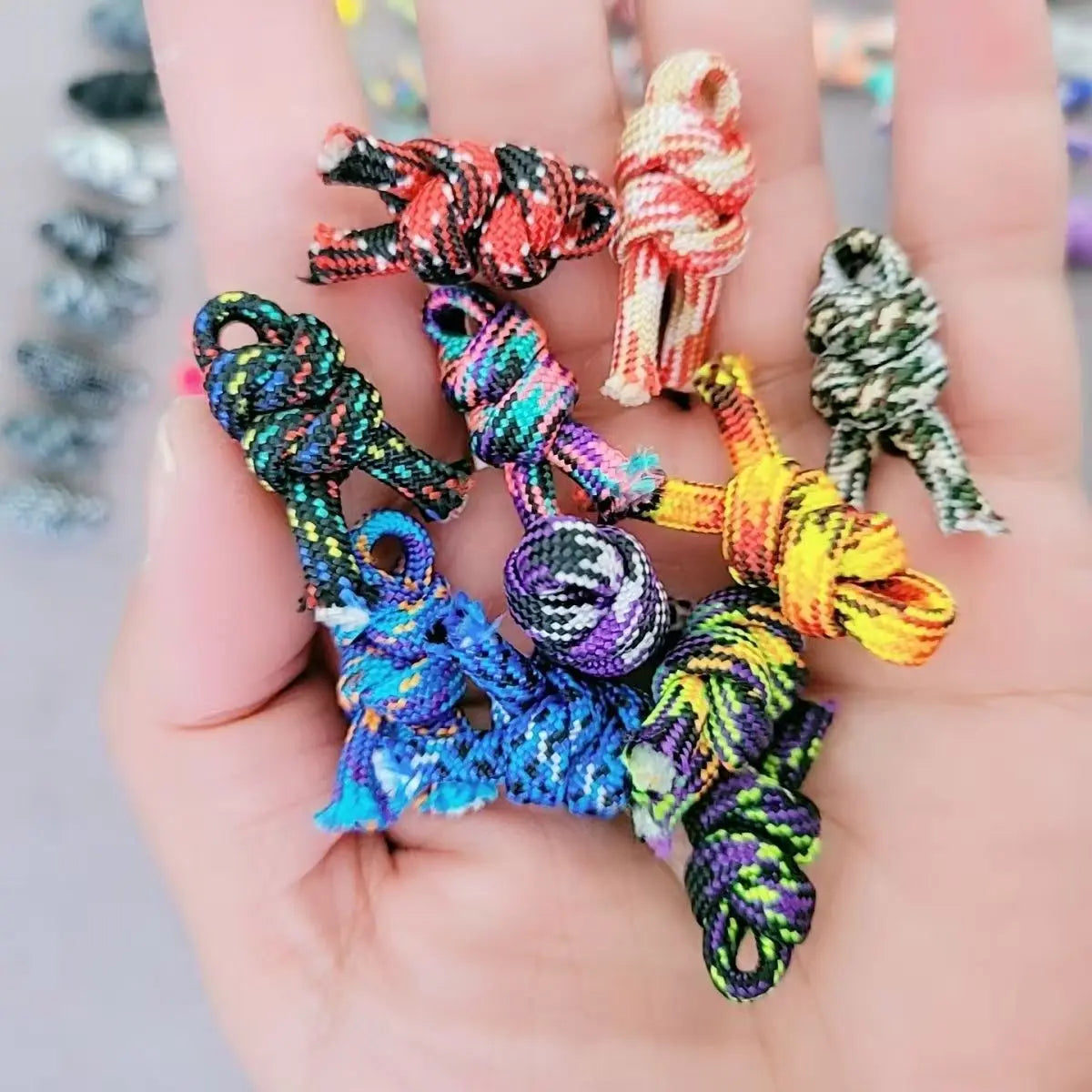 A hand holds several brightly colored paracord ropes with various knots and textures.