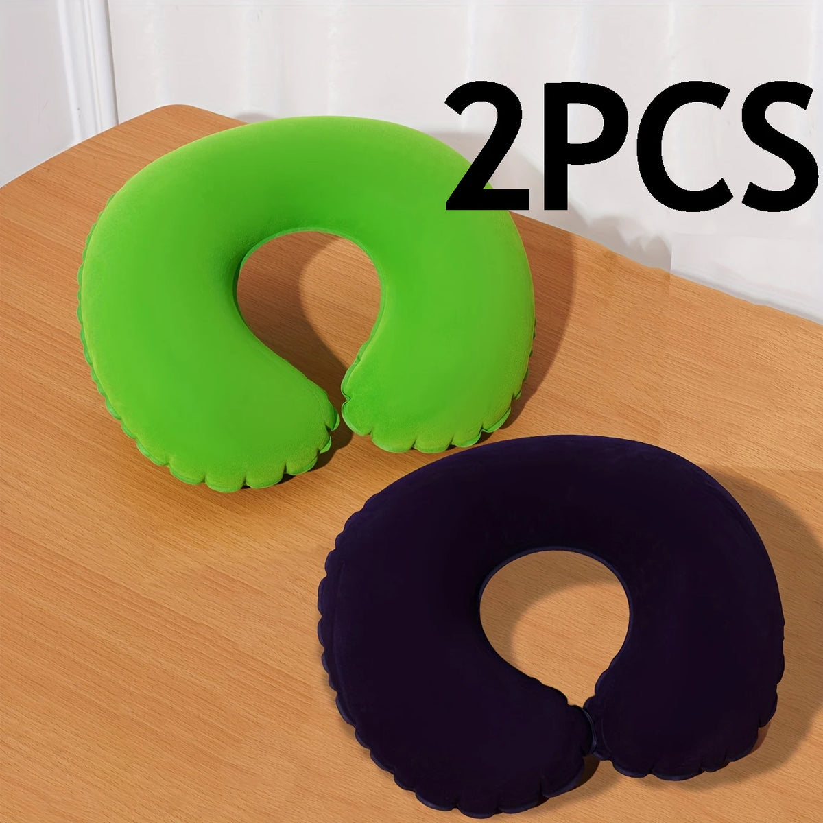Two inflatable U-shaped travel neck pillows, one lime green and one dark purple, resting on a wooden surface.