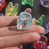 A hand holds a clear acrylic alphabet bead, showing its shape and clarity against a dark background.