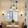 A modern dining room features three crystal pendant lights hanging over a table in front of a window.