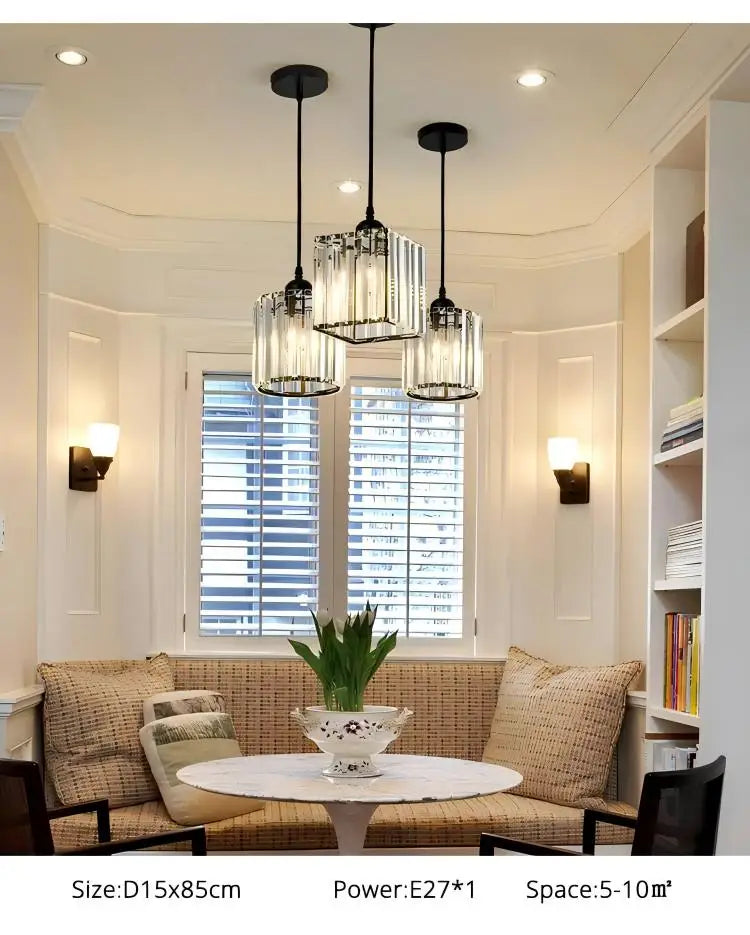 A modern dining room features three crystal pendant lights hanging over a table in front of a window.