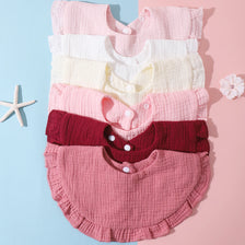 A stack of five soft cotton baby bibs in various shades of pink and white, including a deep red option.