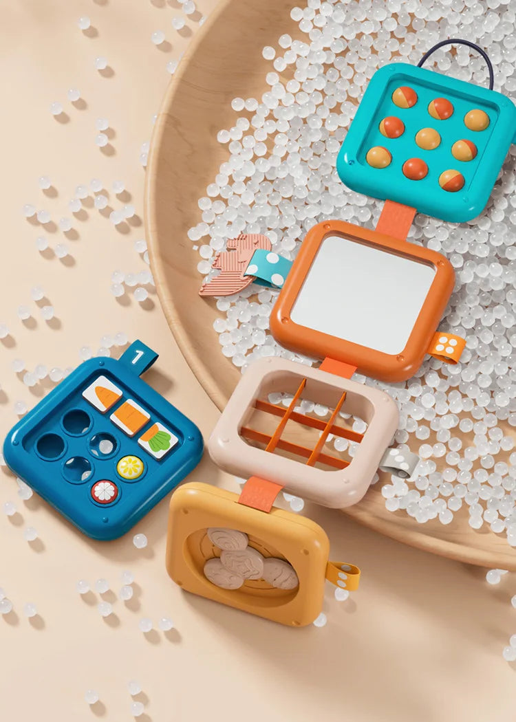 A wooden board features colorful sensory folding activity cubes for toddlers, demonstrating fine motor skills.