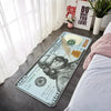 A US $100 banknote lying on a gray floor next to a white bed and sheer curtains.