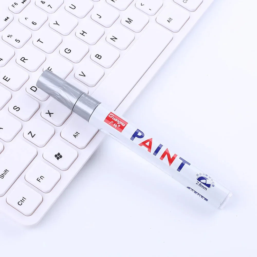 A silver paint marker with a red and blue tip rests on a white computer keyboard.