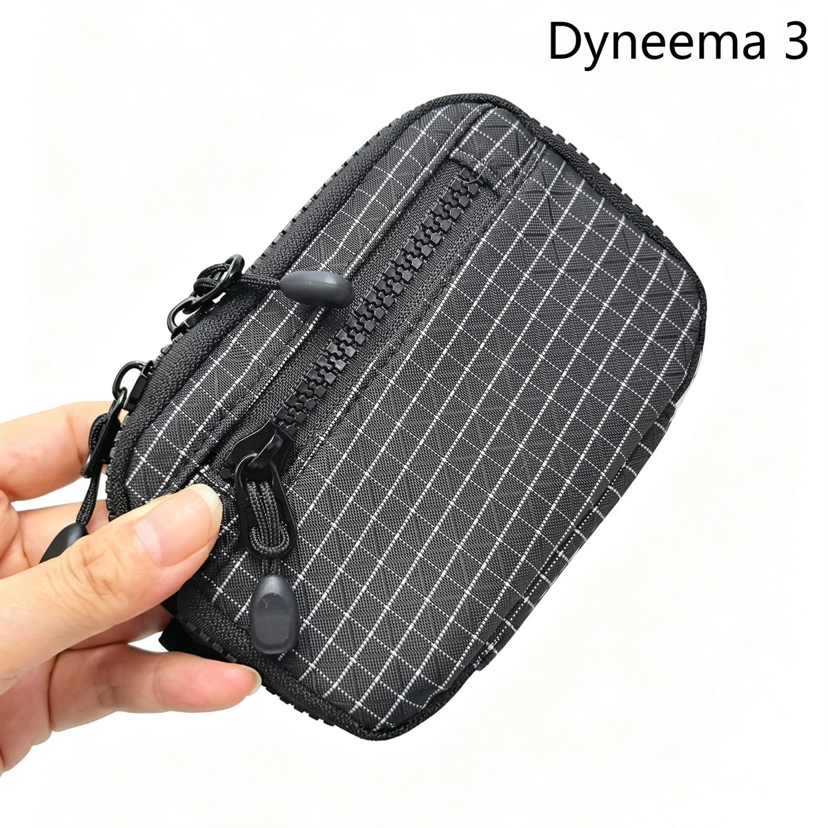 A hand holds a black Dyneema 3 utility pouch featuring a subtle plaid pattern and zippered closure.