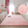 A fluffy pink accent rug is laid on a light wood floor in a bright, minimalist room with sheer curtains.