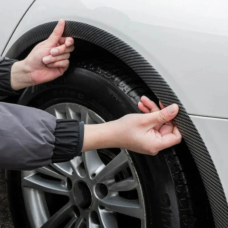 Hands are adjusting carbon fiber-look wheel arch trims on a car wheel.