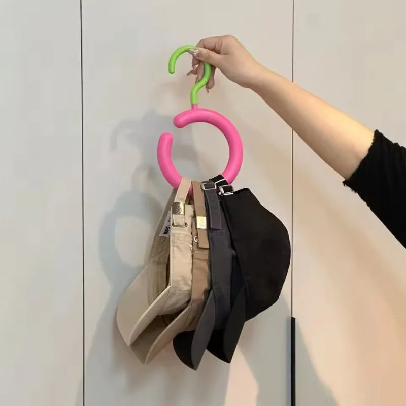 A hand is hanging a green hook onto a wall-mounted organizer featuring various colored hats and scarves.