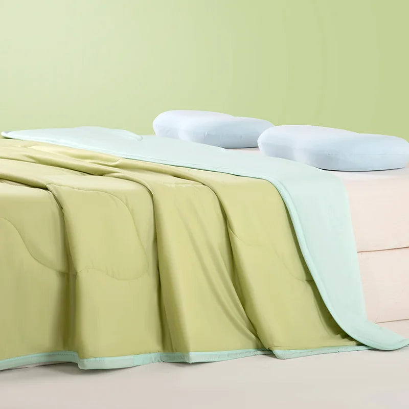 Light green ice silk cooling blanket draped over a bed with white pillows.