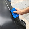 A hand uses a blue suede felt squeegee to apply a vinyl wrap or window tint onto a black surface.