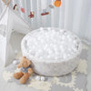 A white ball pit filled with white plastic balls, surrounded by small stuffed bears and a decorative banner.