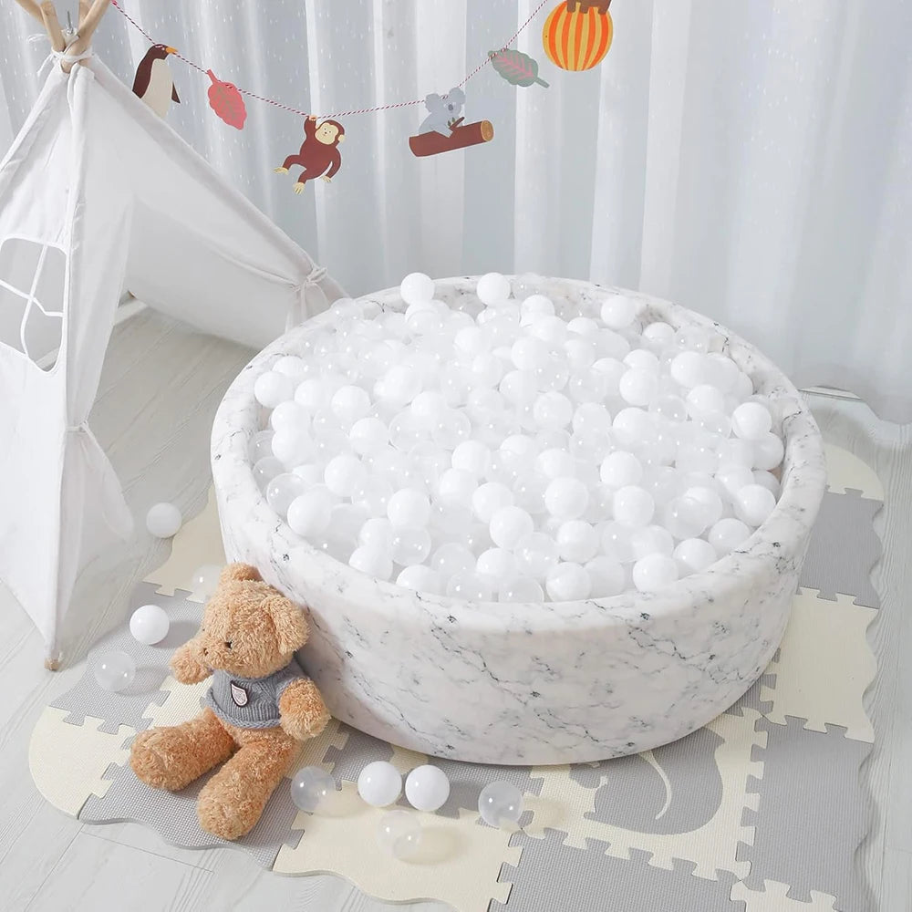 A white ball pit filled with white plastic balls, surrounded by small stuffed bears and a decorative banner.