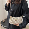 A woman holds a white and gray patterned PU leather crossbody bag with a metal M accent against a dark clothing background.
