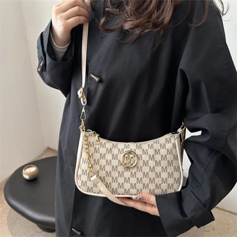 A woman holds a white and gray patterned PU leather crossbody bag with a metal M accent against a dark clothing background.