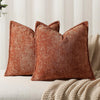 A square, textured, rust-colored chenille decorative cushion cover resting on a light-colored fabric.