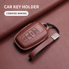 A brown genuine leather car key holder with a black strap is shown on a maroon surface.