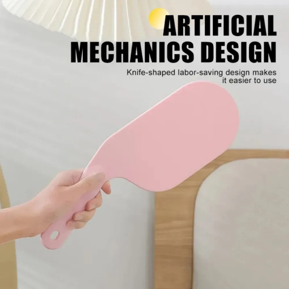 A hand is using a pink knife-shaped fabric tool to tuck or organize a bed sheet.