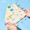 A hand is holding a yellow baby sensory tag comfort blanket with a soothing teether on a light blue surface.