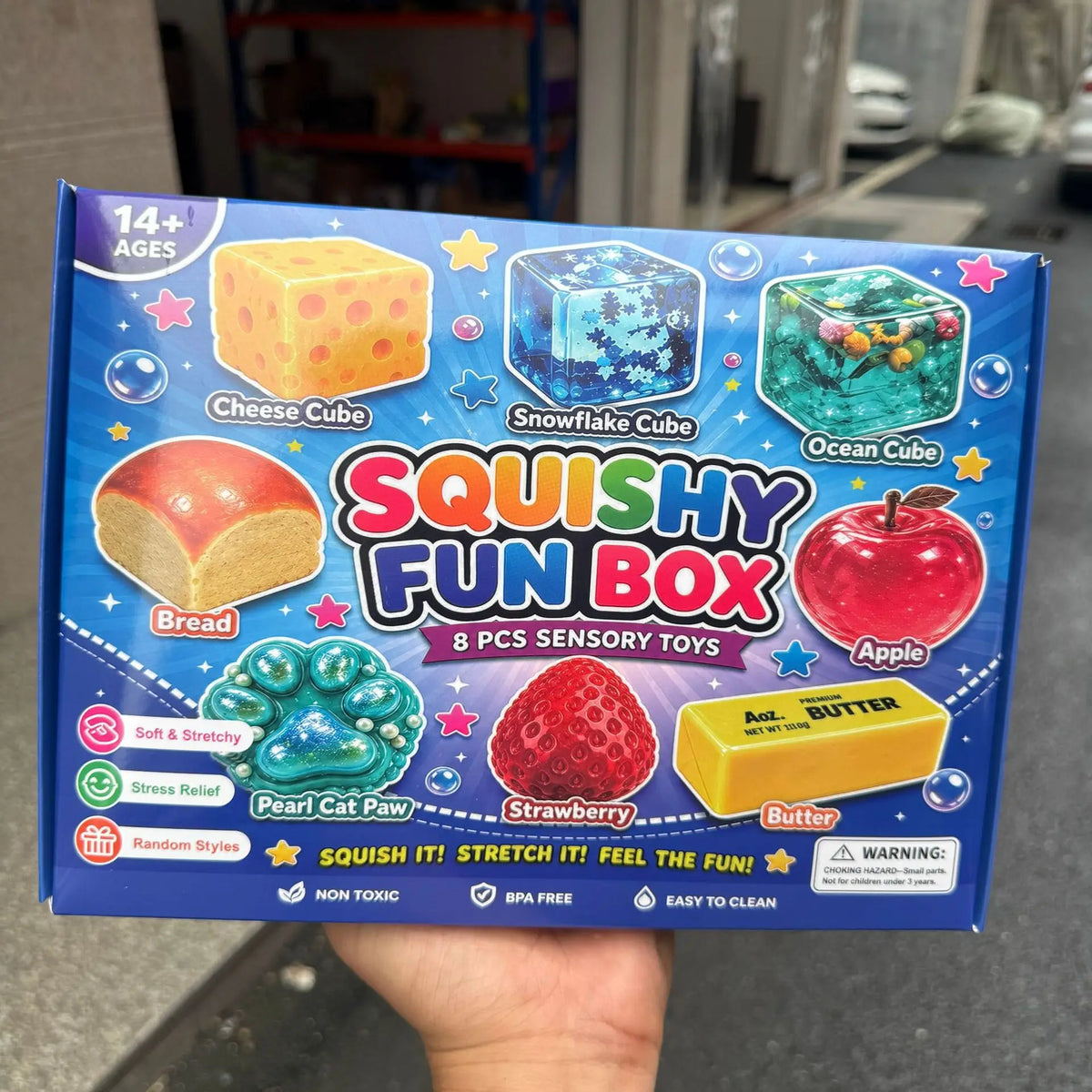 Eine Box mit Squishy Fun Box, die acht sensorische Spielzeuge enthält, darunter Käse-, Schneeflocken-, Ozean-, Brot- und Apfe