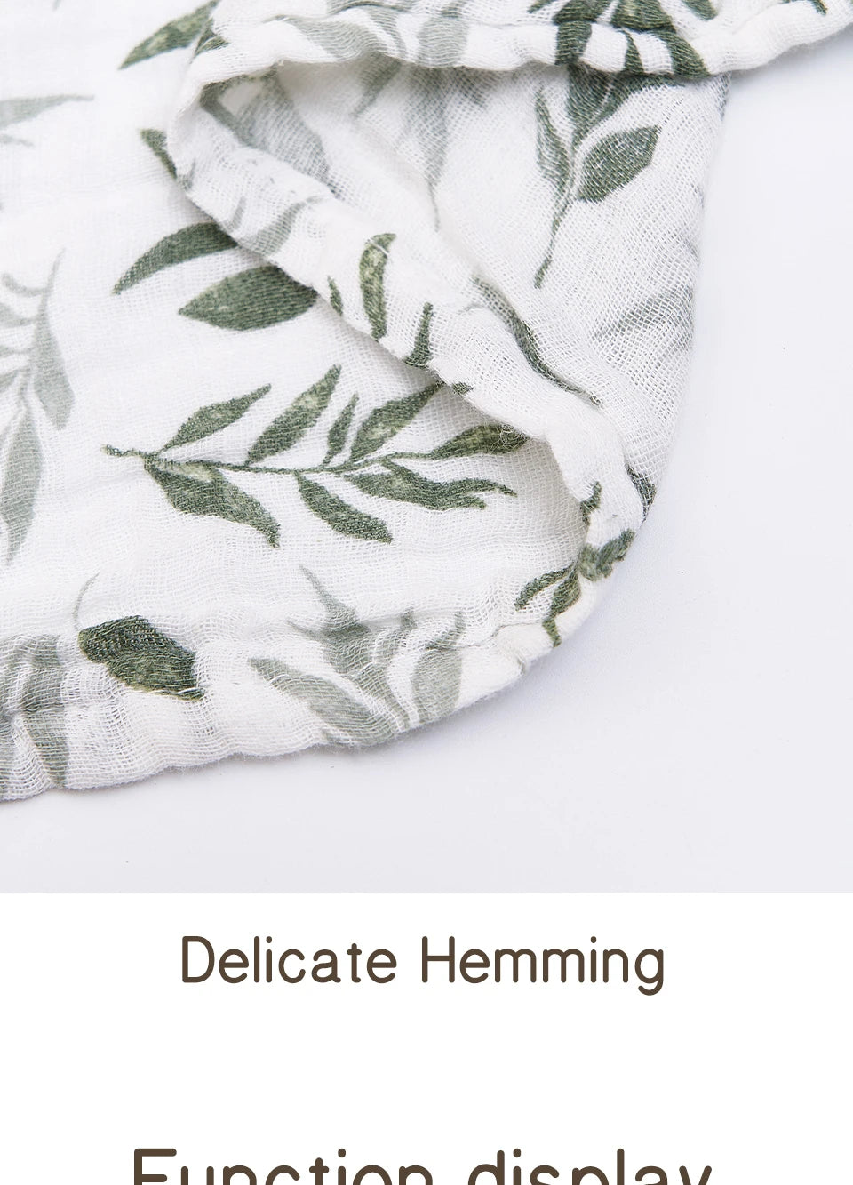 Close-up of a white muslin baby swaddle blanket with green leaf print showing delicate hemming.
