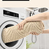 A hand is pulling a beige plush velvet bathroom mat with a non-slip backing out of a white washing machine.