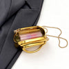 A small gold metal clutch bag with a clear window and a gold chain strap is shown against a dark gray suit jacket.