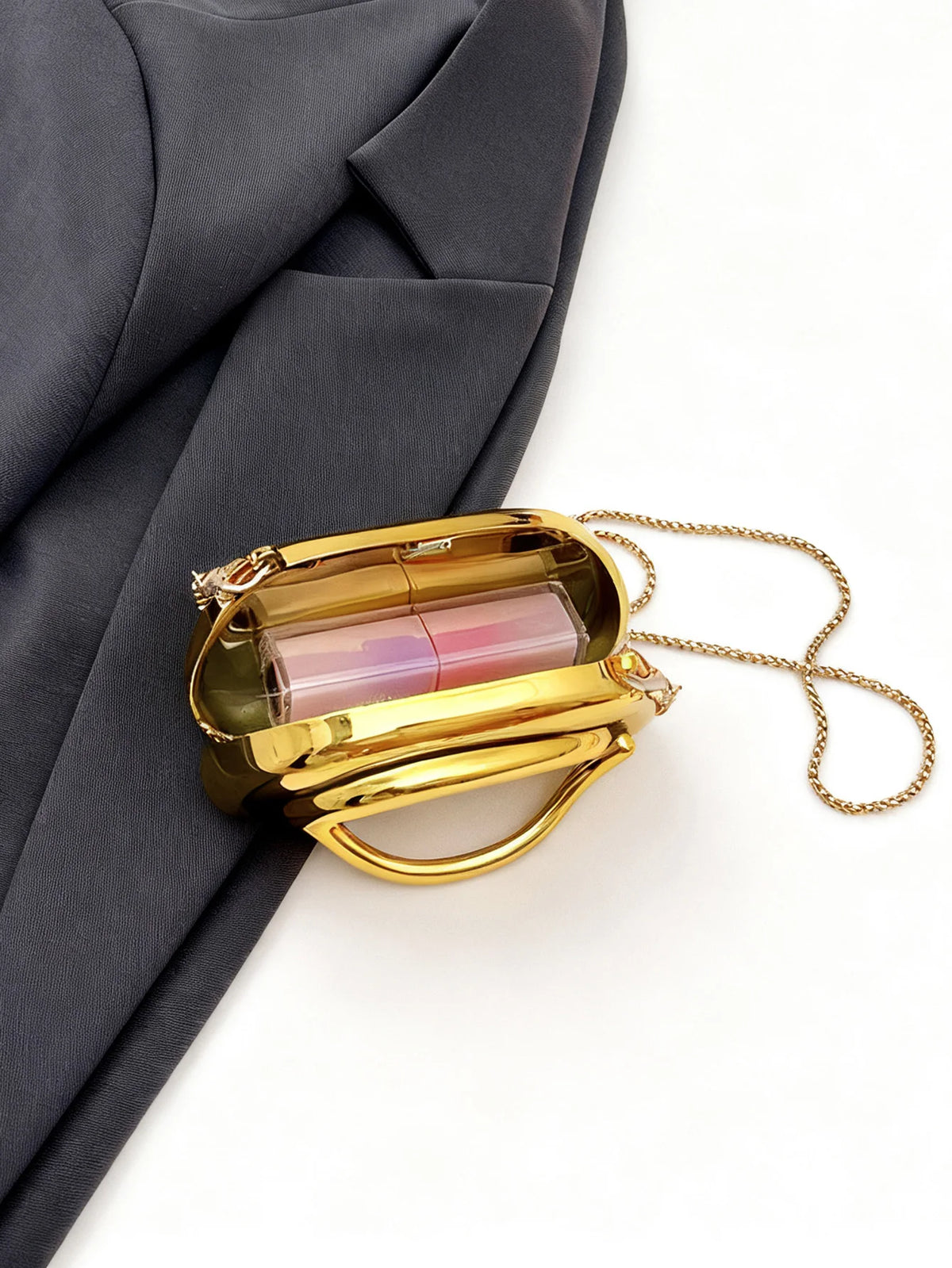 A small gold metal clutch bag with a clear window and a gold chain strap is shown against a dark gray suit jacket.