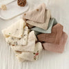 A stack of soft cotton gauze burp cloths in various muted tones including beige, sage green, and dusty rose.