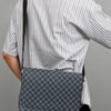 A woman wearing a striped shirt holds a gray patterned crossbody bag on her shoulder.