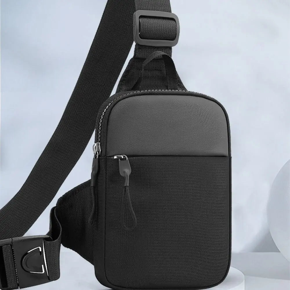 A black compact canvas crossbody sling bag with a strap is shown against a light gray background.