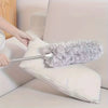 A hand is using an extendable microfiber duster with a flexible head to clean a white pillow.