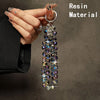 A hand holds a long necklace made of iridescent resin beads against a dark background.