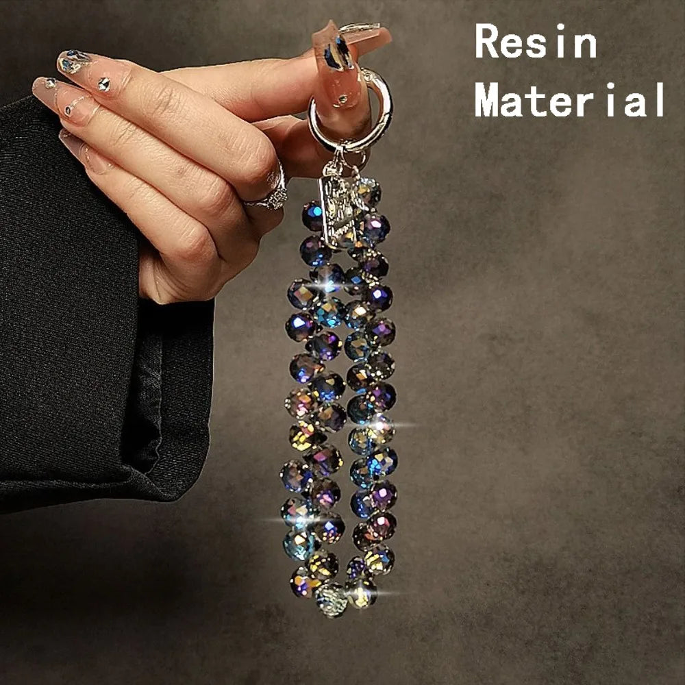 A hand holds a long necklace made of iridescent resin beads against a dark background.