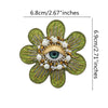 A six-pointed floral patch made of green fabric and adorned with gold and white beads and a central eye design.