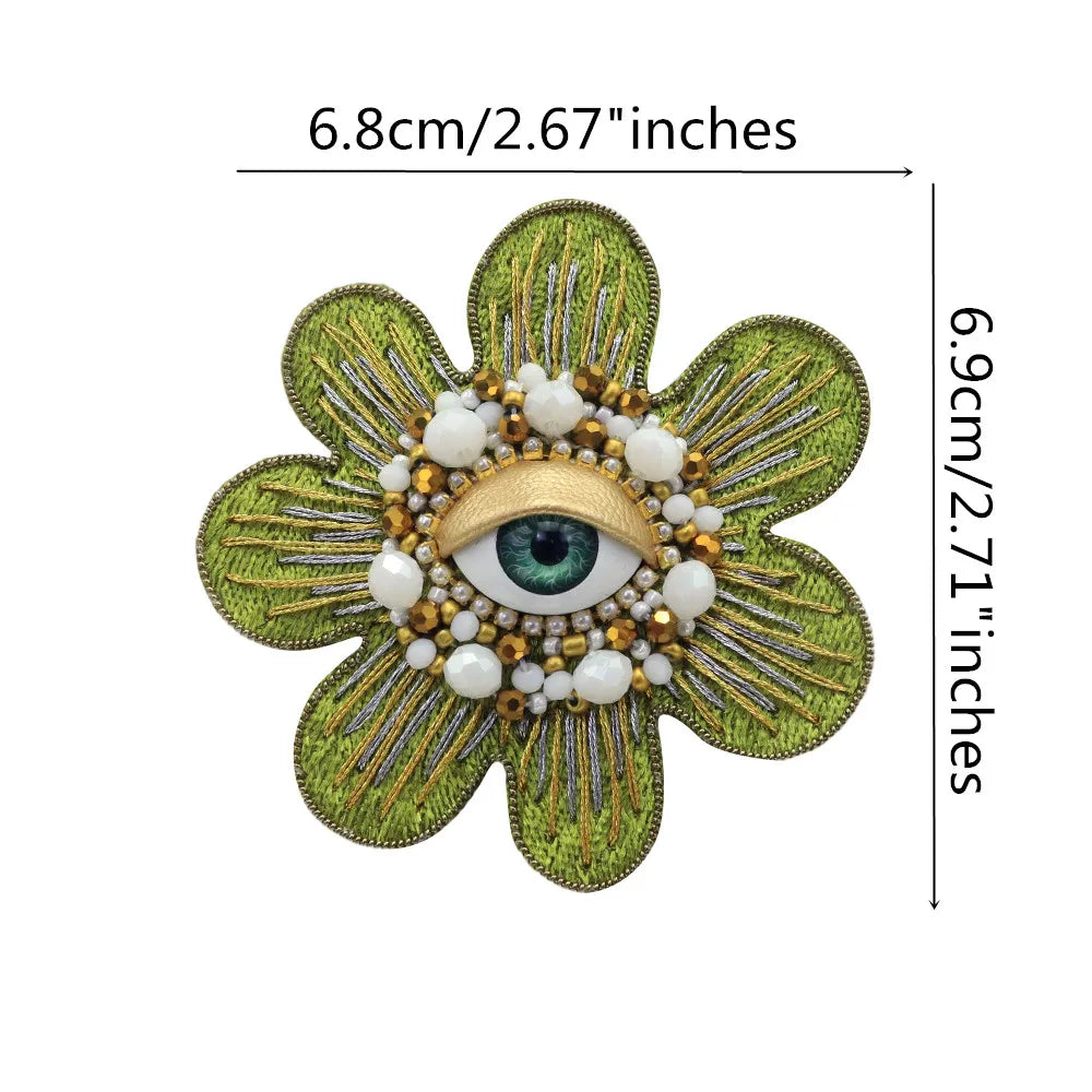 A six-pointed floral patch made of green fabric and adorned with gold and white beads and a central eye design.