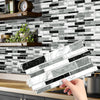 A hand is placing rectangular peel-and-stick tile stickers featuring black and white marble patterns onto a kitchen backsplas